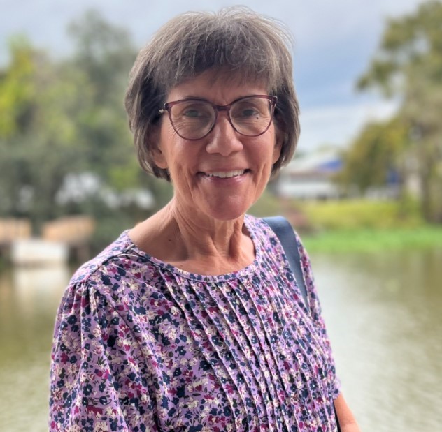 Person standing near water with trees and greenery in the background.